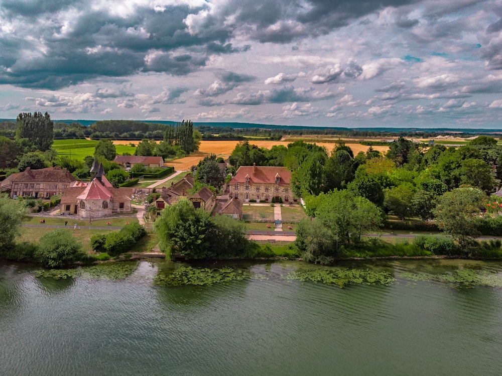 brown and white concrete house near green trees and body of water under white clouds and