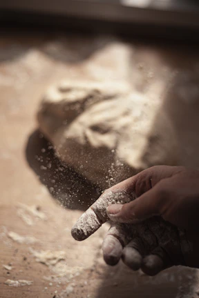 Artisan pizza being hand-stretched with visible texture of the dough and flour dust.