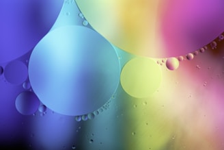 A collection of multicolored circles of various sizes appears against a blurred gradient background. The circles are translucent, allowing the layered colors to blend harmoniously, creating a soft, abstract composition. The color palette includes shades of purple, blue, pink, yellow, and green.