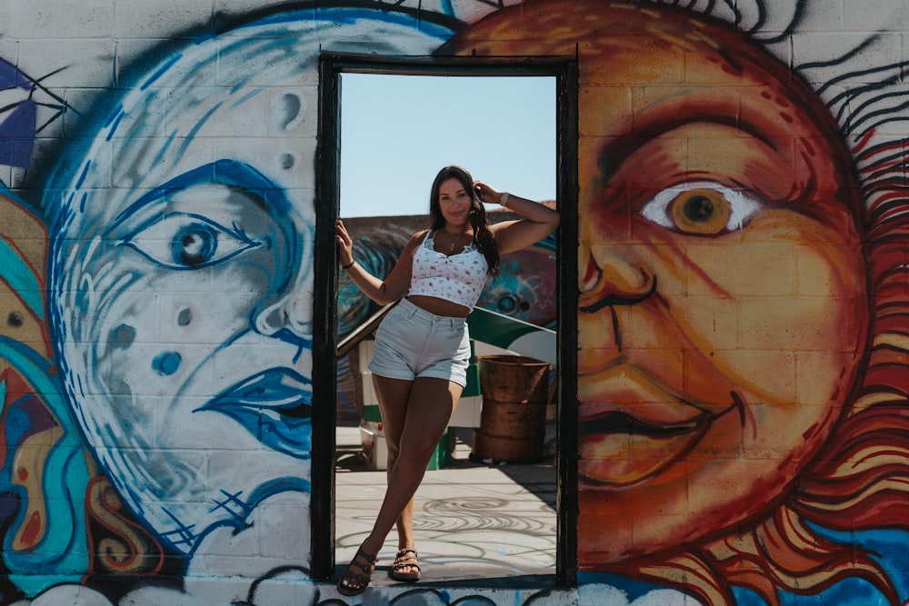 woman in white and black stripe tank top and white shorts standing beside wall with graffiti