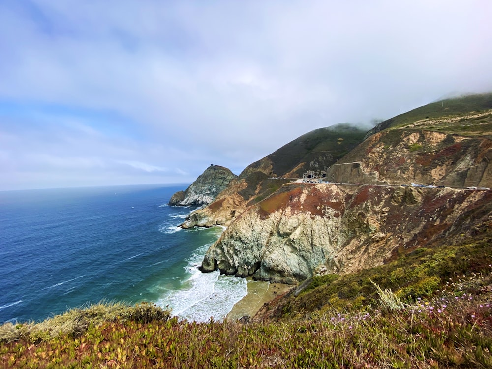 green and brown mountain beside blue sea under blue sky during daytime