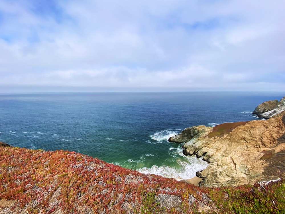 green and brown mountain beside sea under white clouds and blue sky during daytime