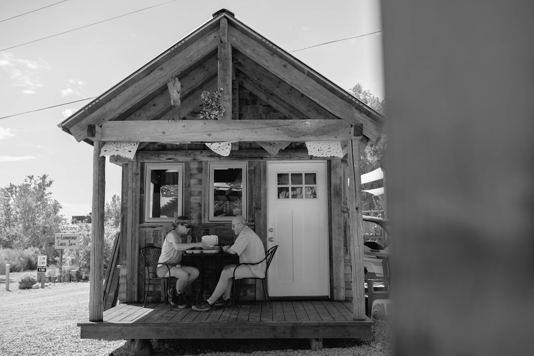 grayscale photo of 2 men sitting on bench in front of house