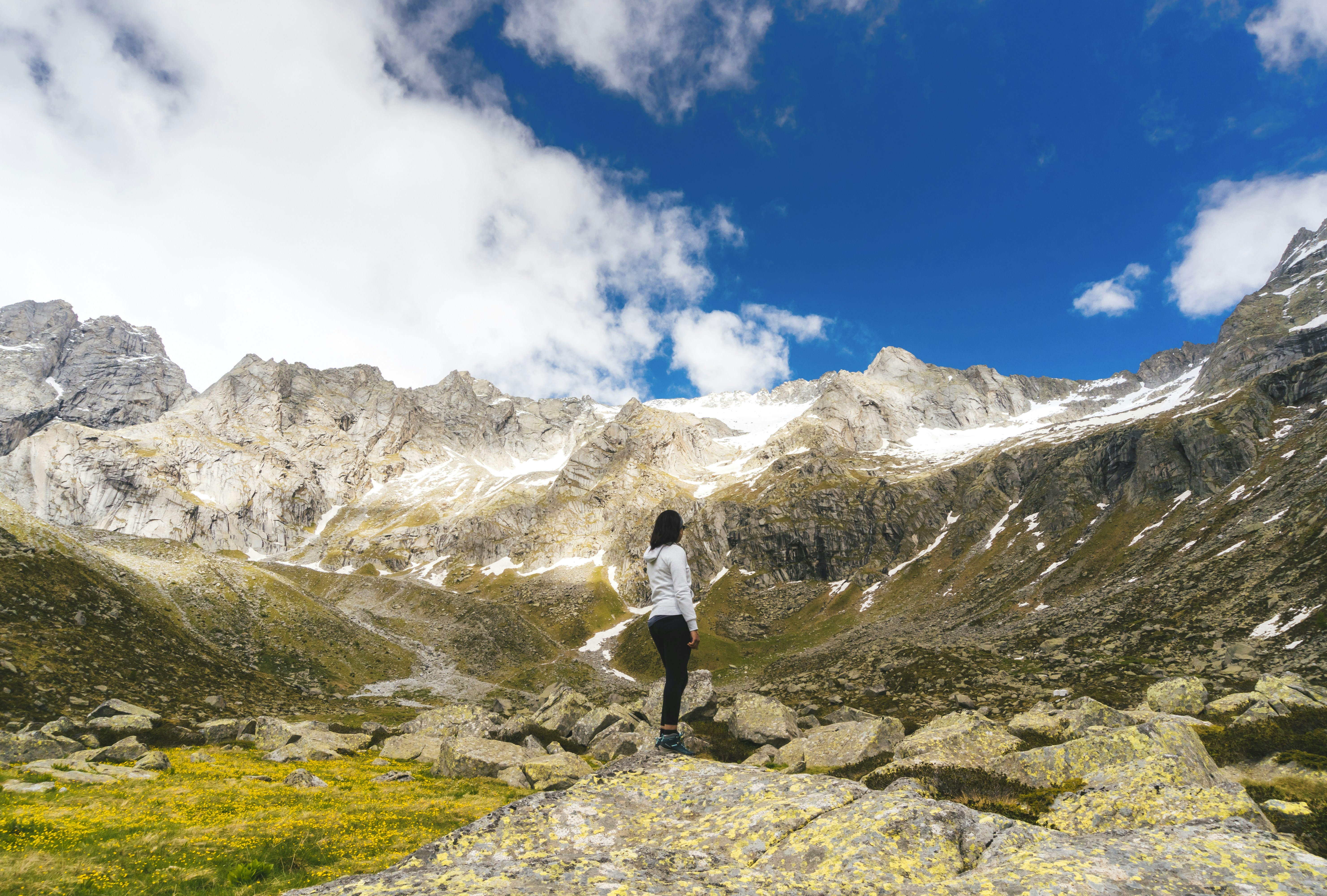 man in white t-shirt and black shorts standing on rocky mountain under white clouds and