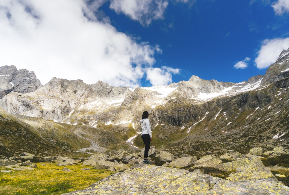 man in white t-shirt and black shorts standing on rocky mountain under white clouds and