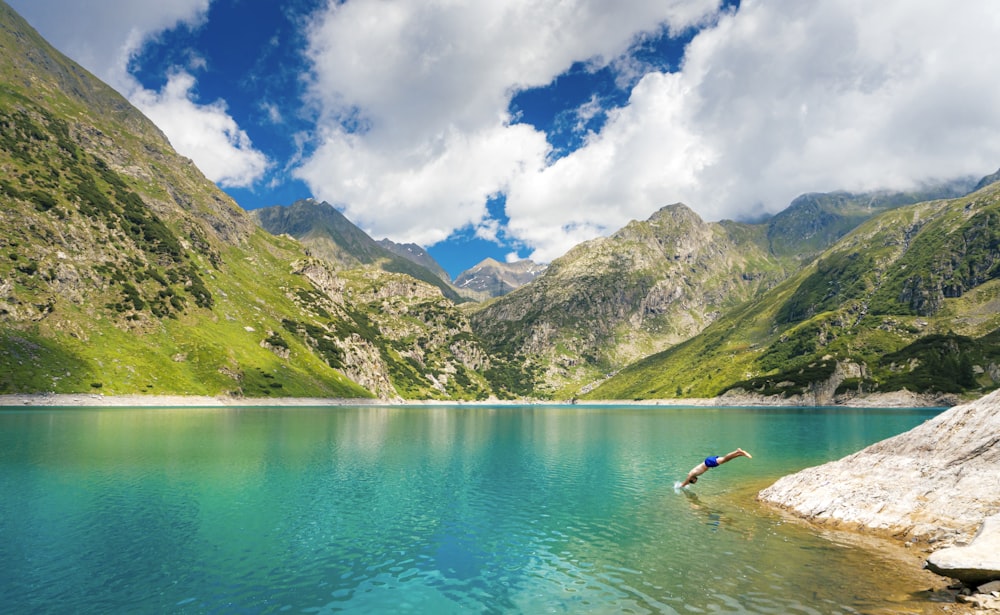 person in blue water near green mountains during daytime