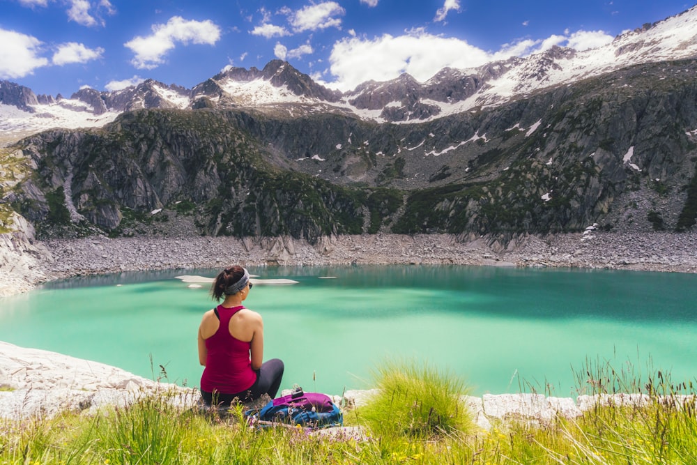 Donna in canotta nera che si siede sull'erba verde vicino al lago durante il giorno