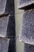 Close-up view of a textured wall composed of dark gray rectangular concrete blocks partially overlapping each other. The blocks are stacked in a staggered pattern creating a three-dimensional effect.