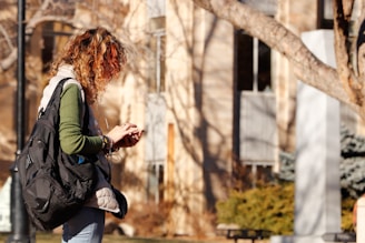 woman in green long sleeve shirt and black pants standing near brown tree during daytime