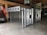 A metal storage or transport crate with a diamond plate pattern is situated in a garage. The crate is constructed from aluminum, featuring a sturdy frame with a grid-like design and handles on the sides.
