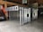 A metal storage or transport crate with a diamond plate pattern is situated in a garage. The crate is constructed from aluminum, featuring a sturdy frame with a grid-like design and handles on the sides.