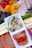 A charcuterie board featuring an assortment of foods, including sliced strawberries, dried apricots, figs, and salami. There is also a section with cheese slices and cured meat. Centrally placed is a dish with marinated artichoke hearts and roasted red peppers.