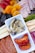 A charcuterie board featuring an assortment of foods, including sliced strawberries, dried apricots, figs, and salami. There is also a section with cheese slices and cured meat. Centrally placed is a dish with marinated artichoke hearts and roasted red peppers.