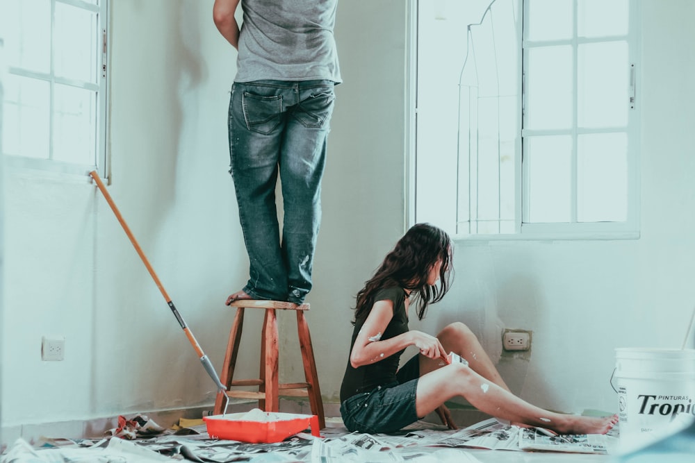 Frau in grauem Tanktop und blauer Jeans sitzt auf dem Bett