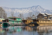 green and brown wooden house on lake near snow covered mountain during daytime