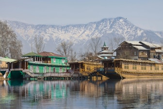green and brown wooden house on lake near snow covered mountain during daytime