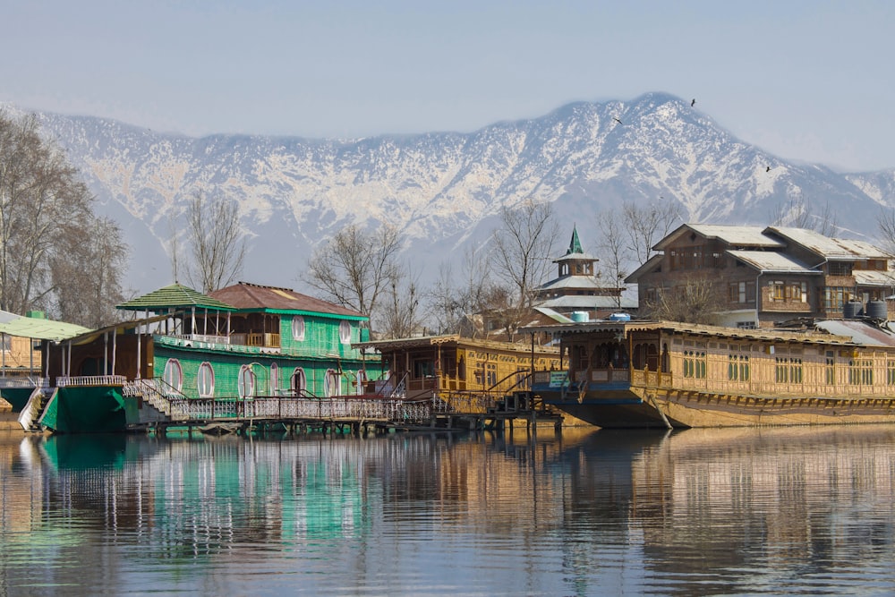 green and brown wooden house on lake near snow covered mountain during daytime