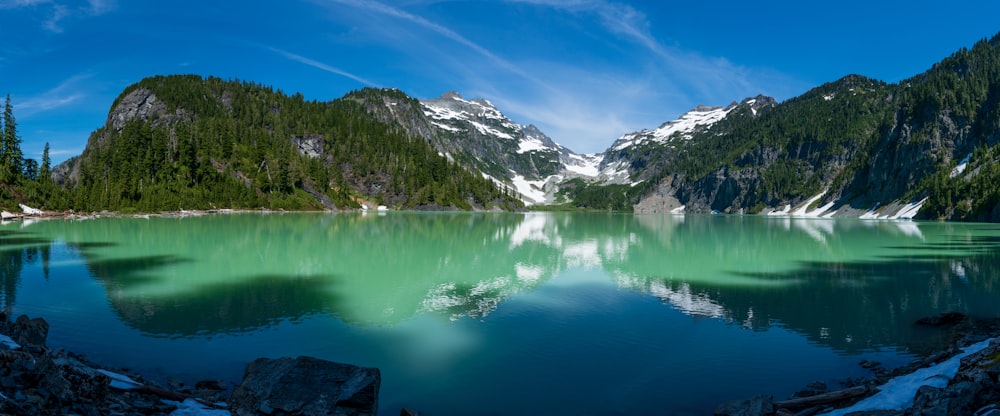 Lago circondato da alberi verdi e montagne innevate durante il giorno