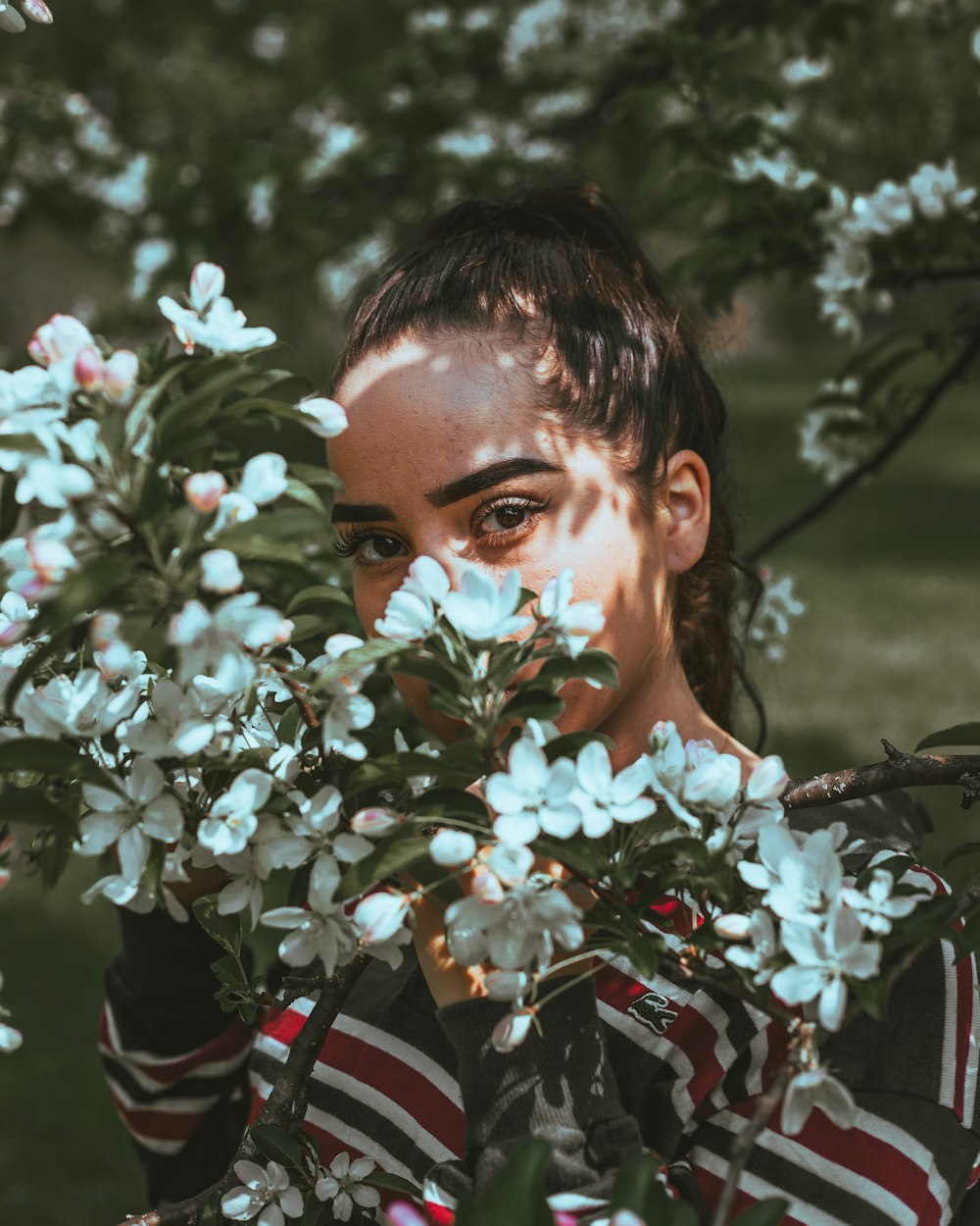 woman in white floral shirt standing beside white flowers during daytime