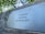 A metal plaque is mounted on a weathered wooden surface, bearing the inscription 'In Liefdevolle herinnering 1931 Martien 2007' in a serif font. The background consists of blurred green foliage, suggesting an outdoor setting.