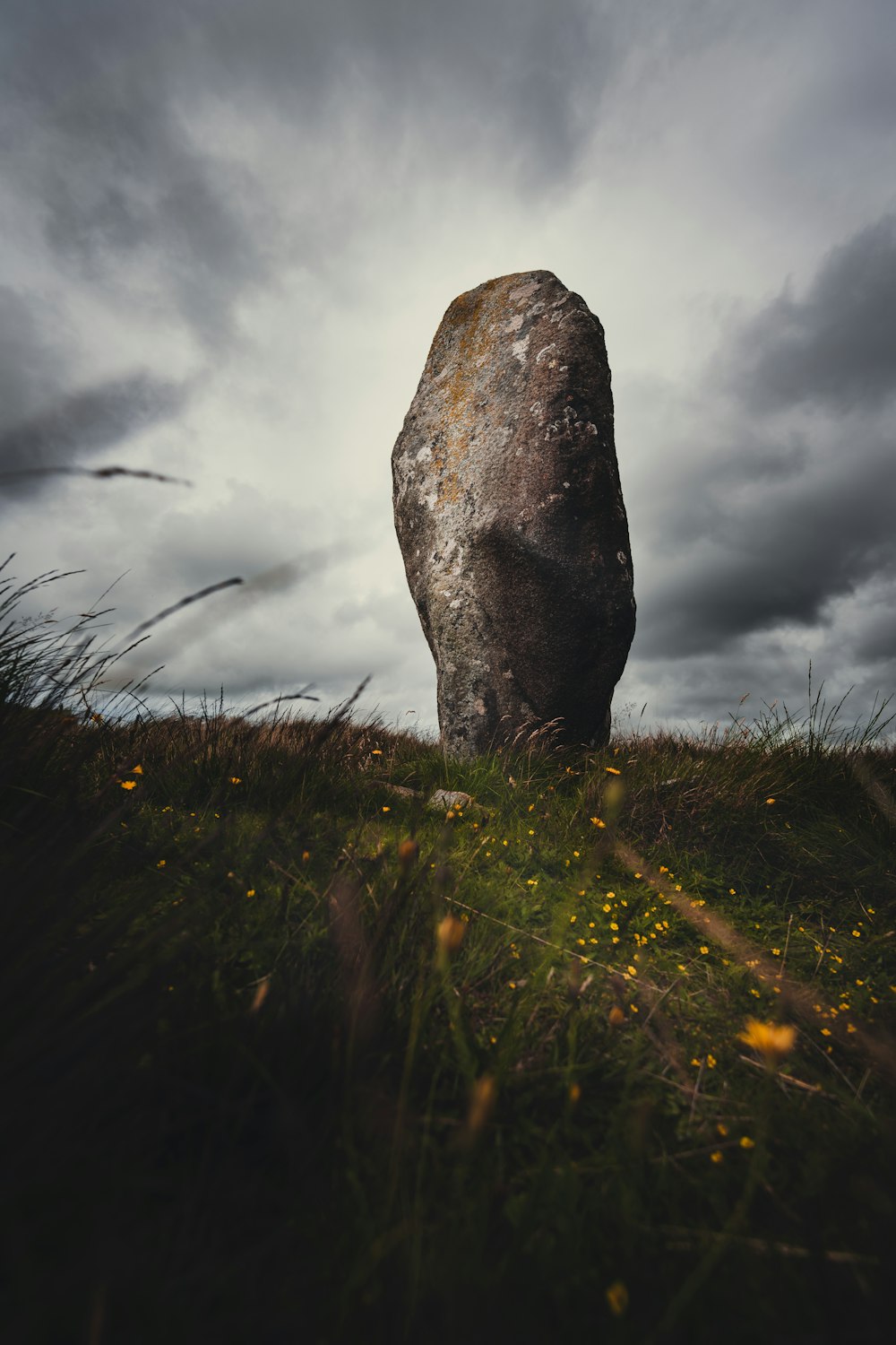 gray rock formation on green grass field under white clouds during daytime