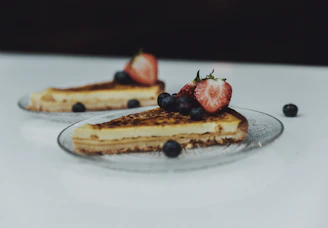 Hands serving a beautifully decorated cake topped with fresh berries on a brown ceramic plate