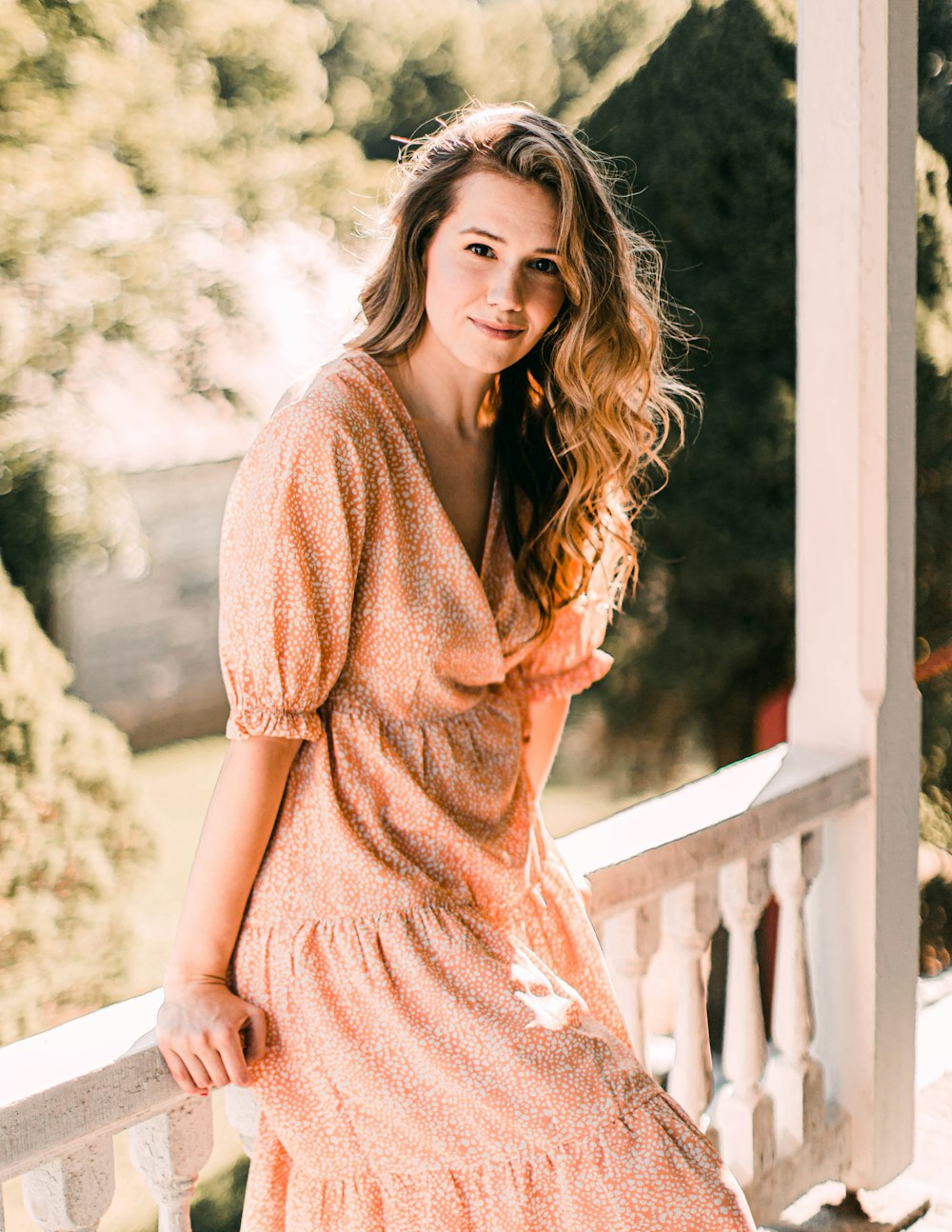 woman in brown dress standing near white wooden fence during daytime