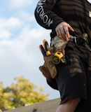 person in black leather jacket holding brown and black hiking shoes