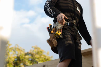 A person in a black long-sleeved shirt wearing a leather tool belt with tape measure