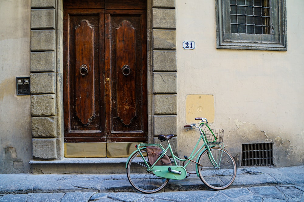green city bicycle beside brown wooden door