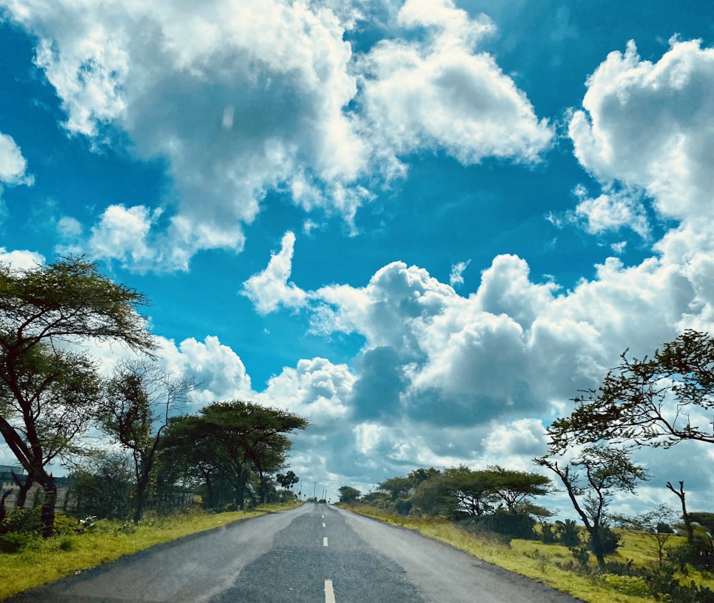 Carretera de asfalto gris entre el campo de hierba verde bajo el cielo nublado soleado azul y blanco durante el día
