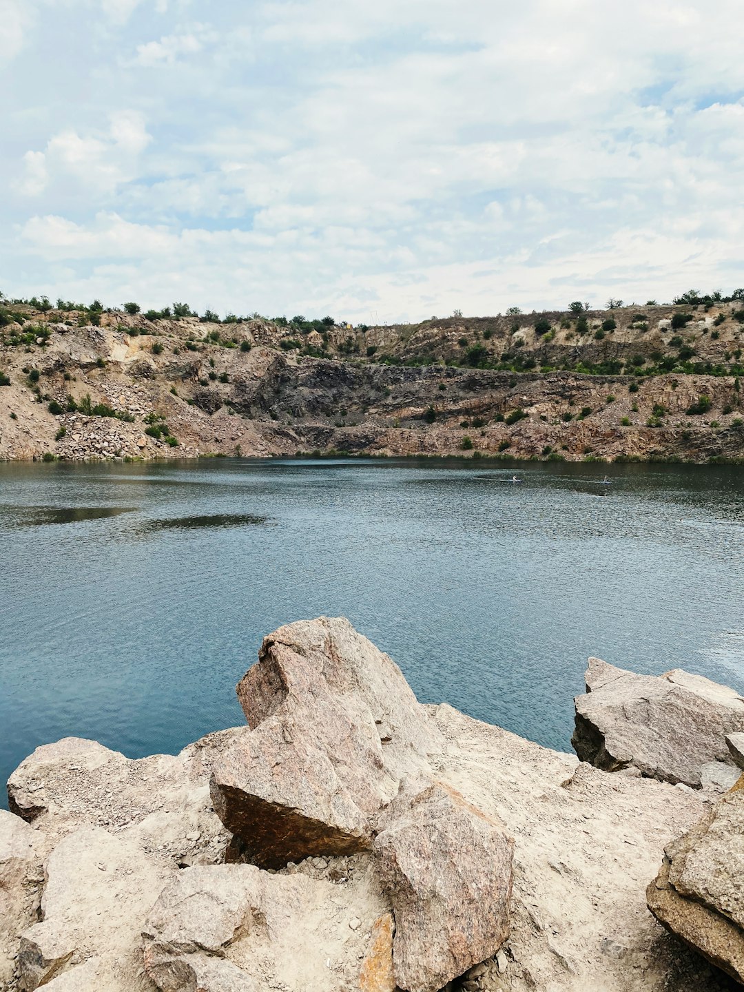 blue lake surrounded by brown rocky mountain under blue and white sunny cloudy sky during daytime