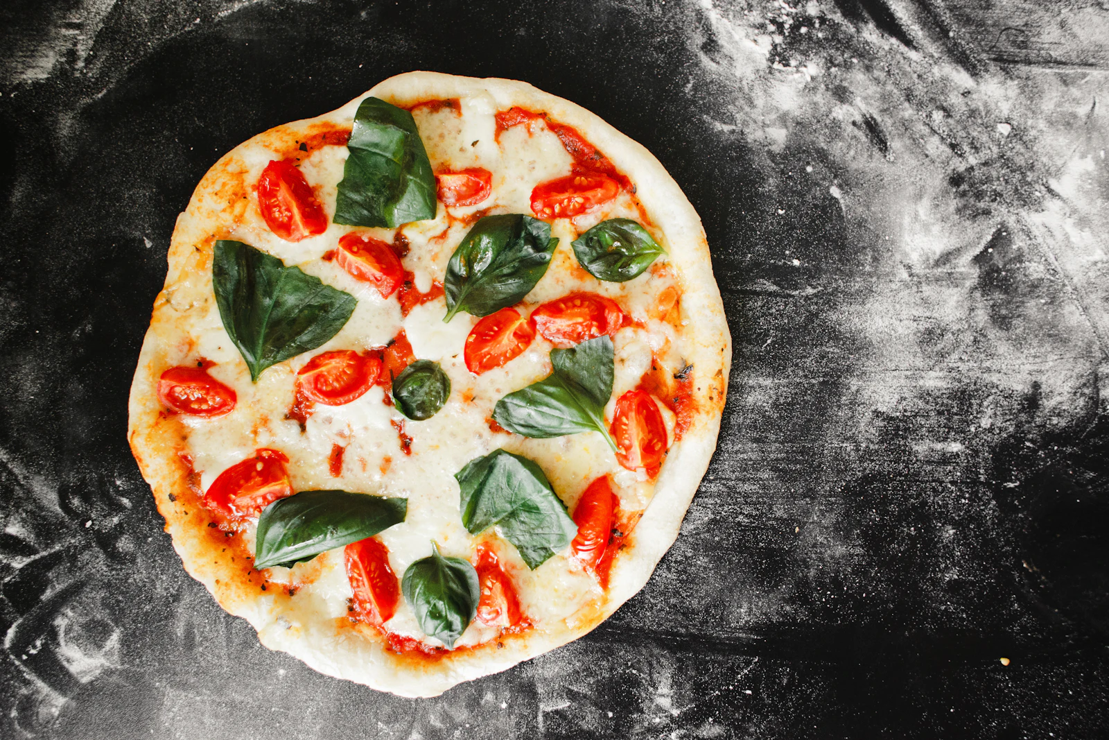 Pizza margherita entière posée sur une surface sombre, mozzarella et basilic frais
