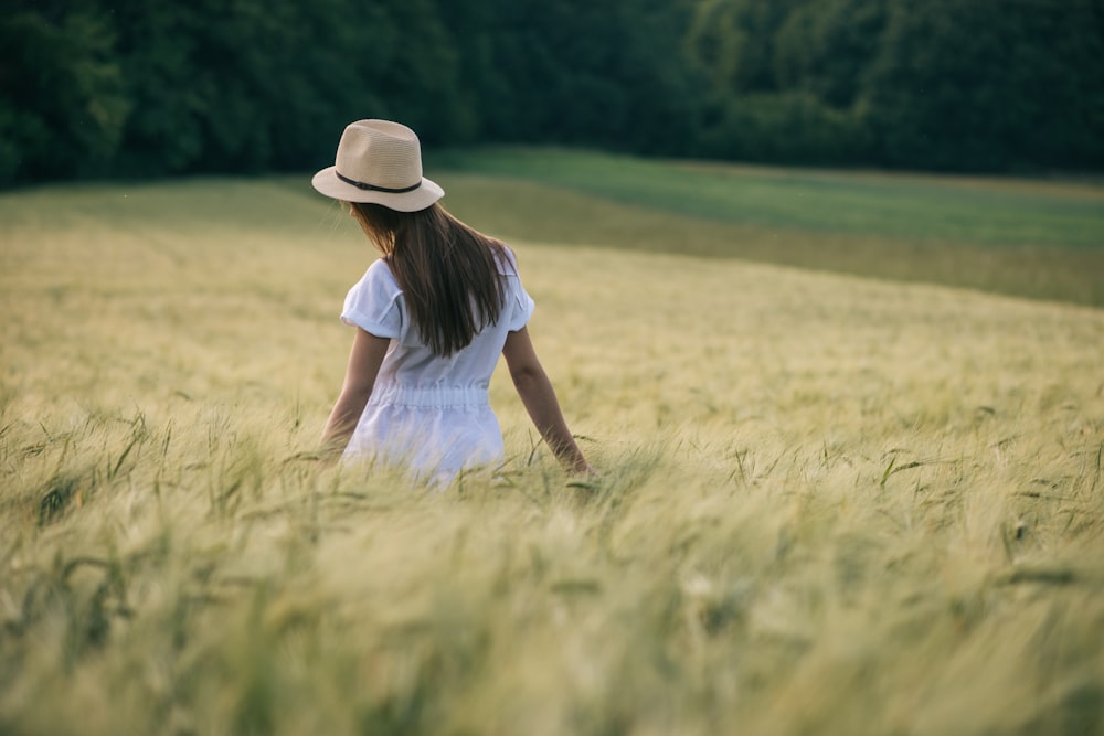 woman in white shirt and brown hat sitting on green grass field during daytime