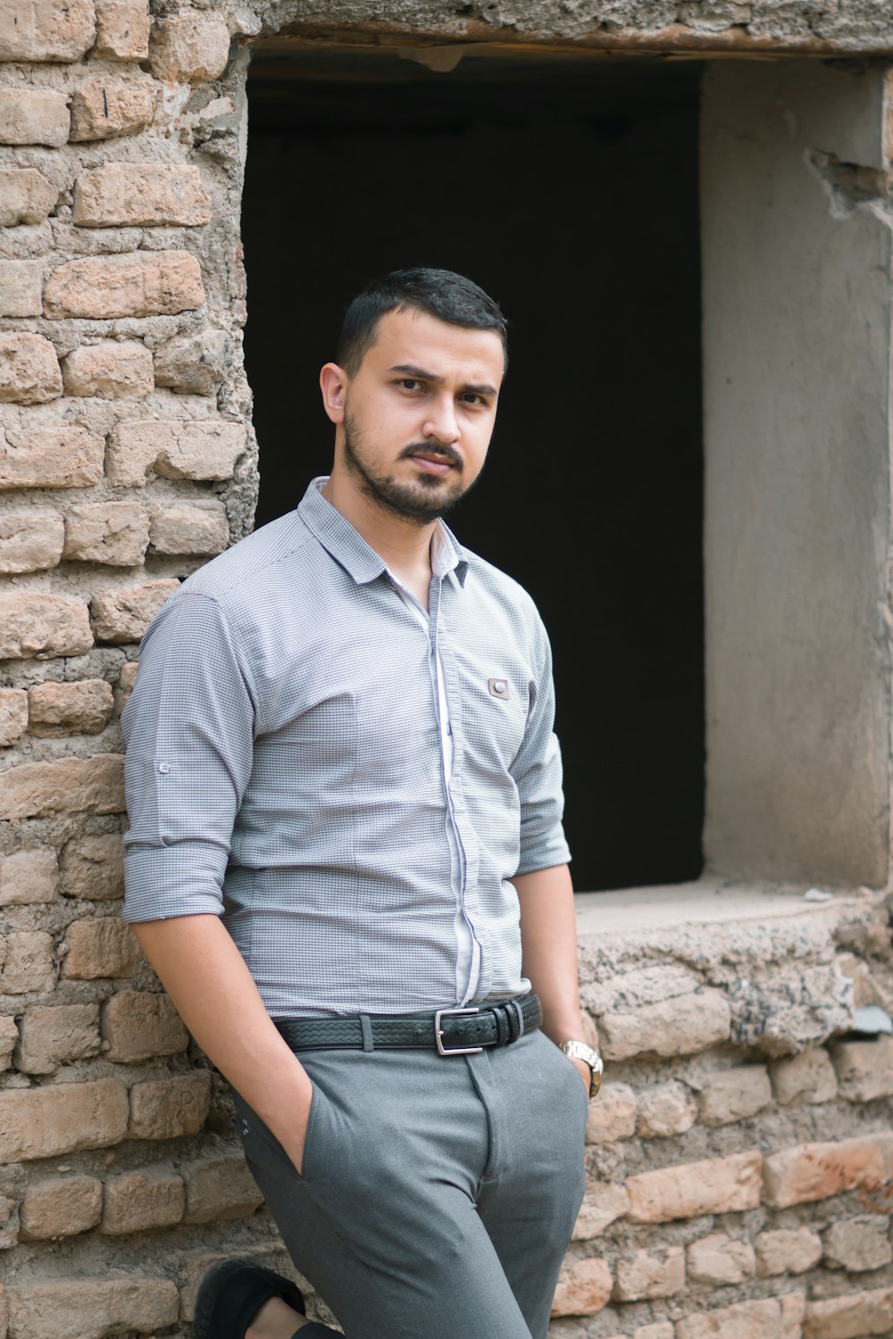 man in gray dress shirt and black denim jeans standing beside brown brick wall during daytime