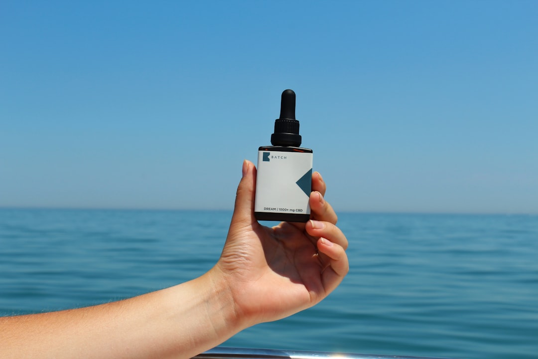 Hand holding CBD oil tincture with sea horizon in the distance