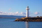 white lighthouse on brown rock formation near body of water during daytime