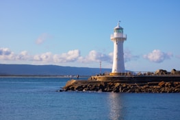 white lighthouse on brown rock formation near body of water during daytime