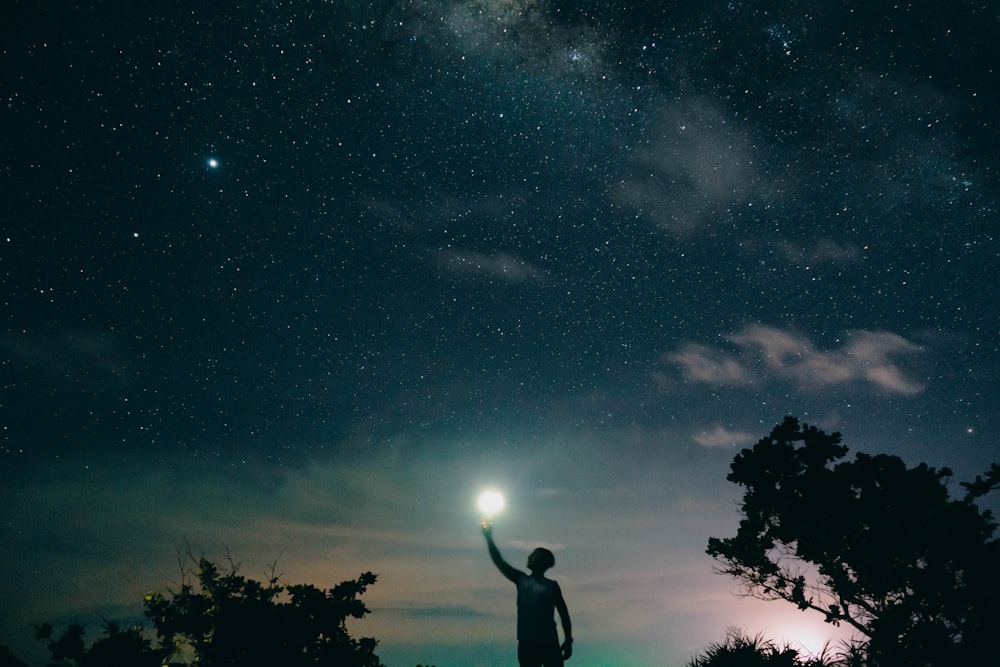 man in black tank top standing near tree under starry night