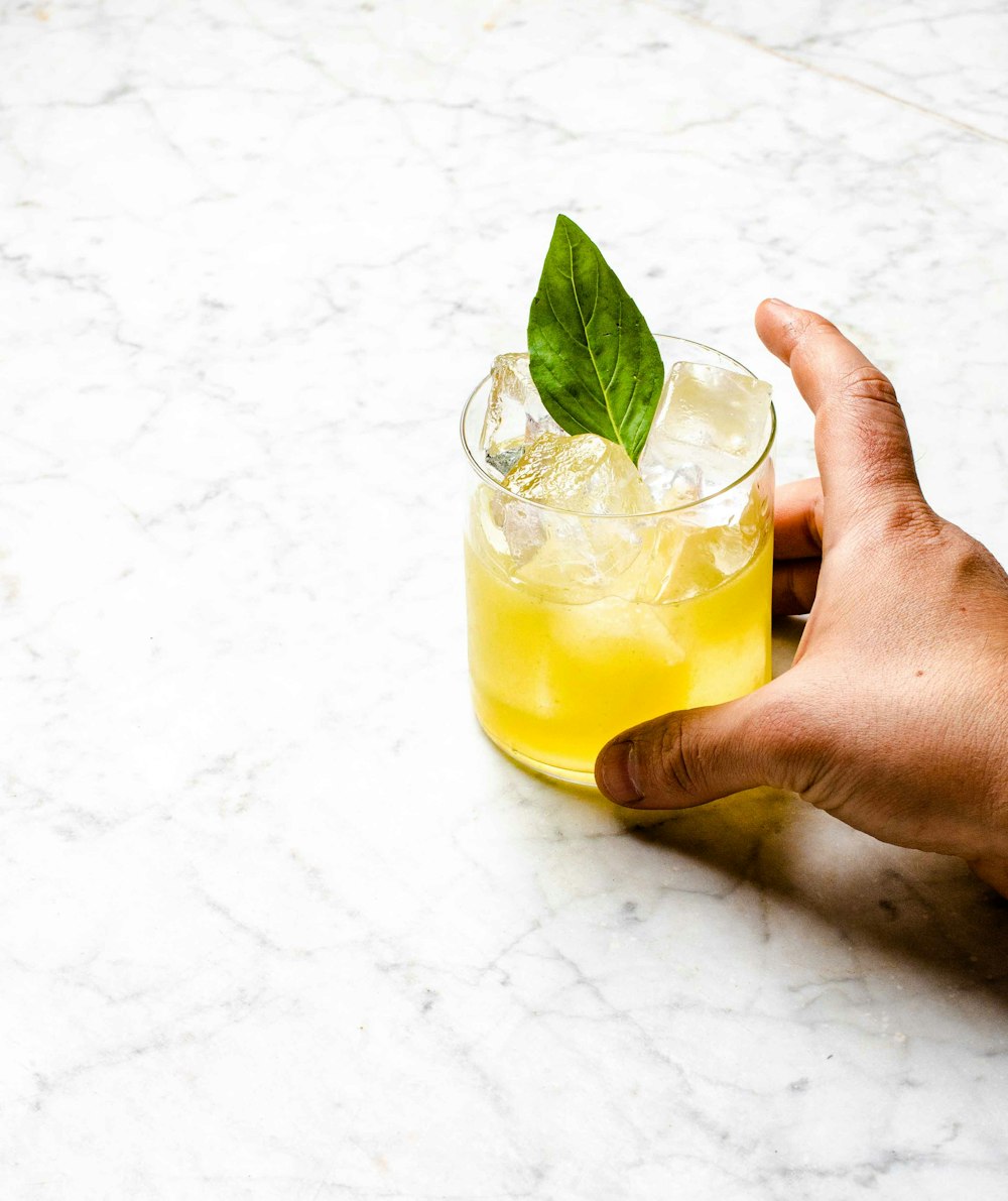 person holding clear drinking glass with yellow liquid