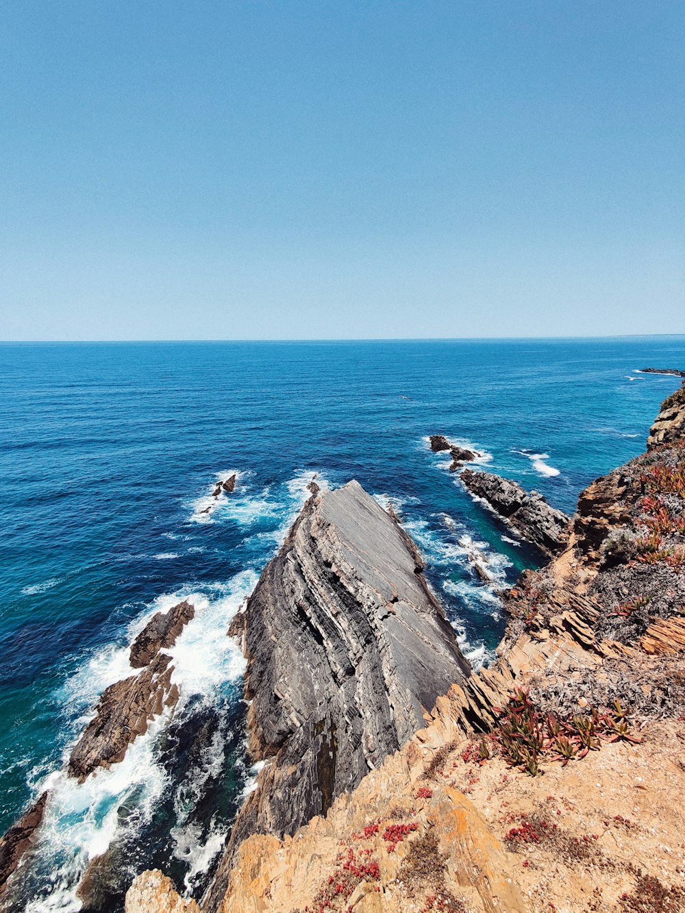 brown rocky mountain beside blue sea under blue sky during daytime