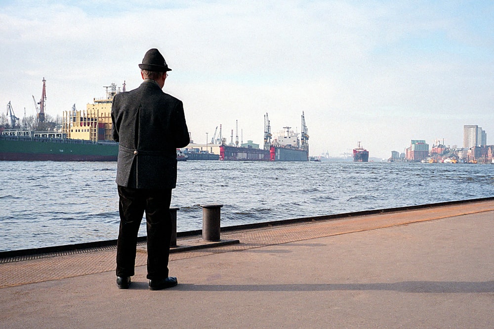 a man in a suit and hat looking out at the water
