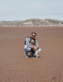 a man kneeling down with a dog on a beach