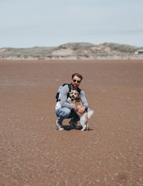 a man kneeling down with a dog on a beach