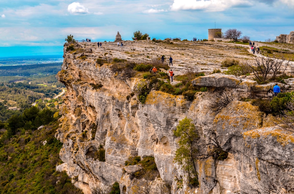 Menschen, die tagsüber unter weißen Wolken auf den braunen Rocky Mountain klettern