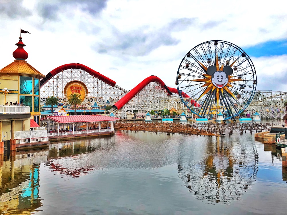 red and white ferris wheel near body of water under cloudy sky during daytime