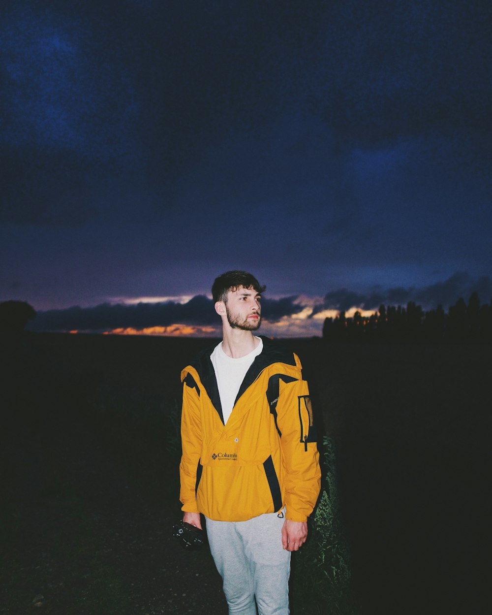 man in yellow jacket standing near body of water during night time