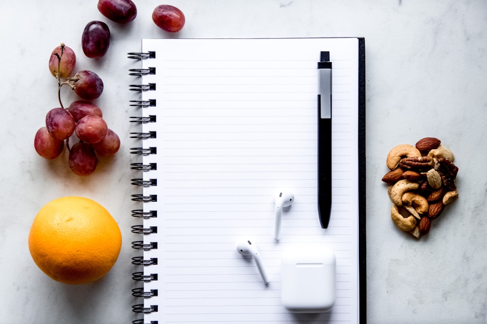 a notepad, pen, fruit, and a charger on a table