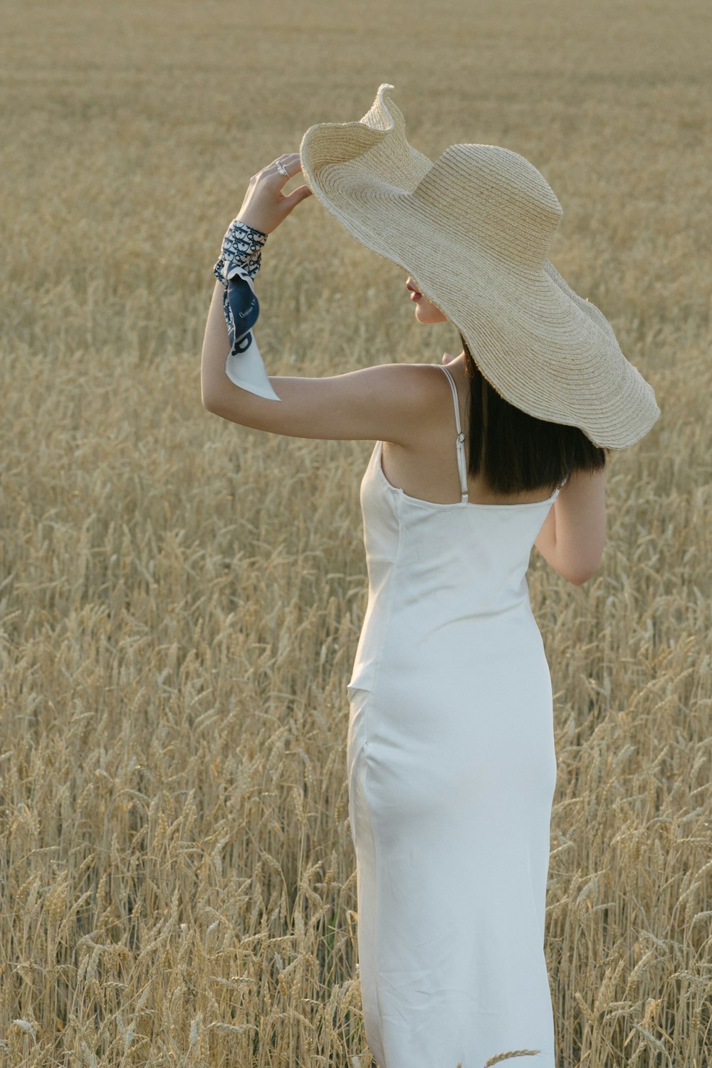 Frau in weißem ärmellosem Kleid, die tagsüber auf braunem Rasen steht