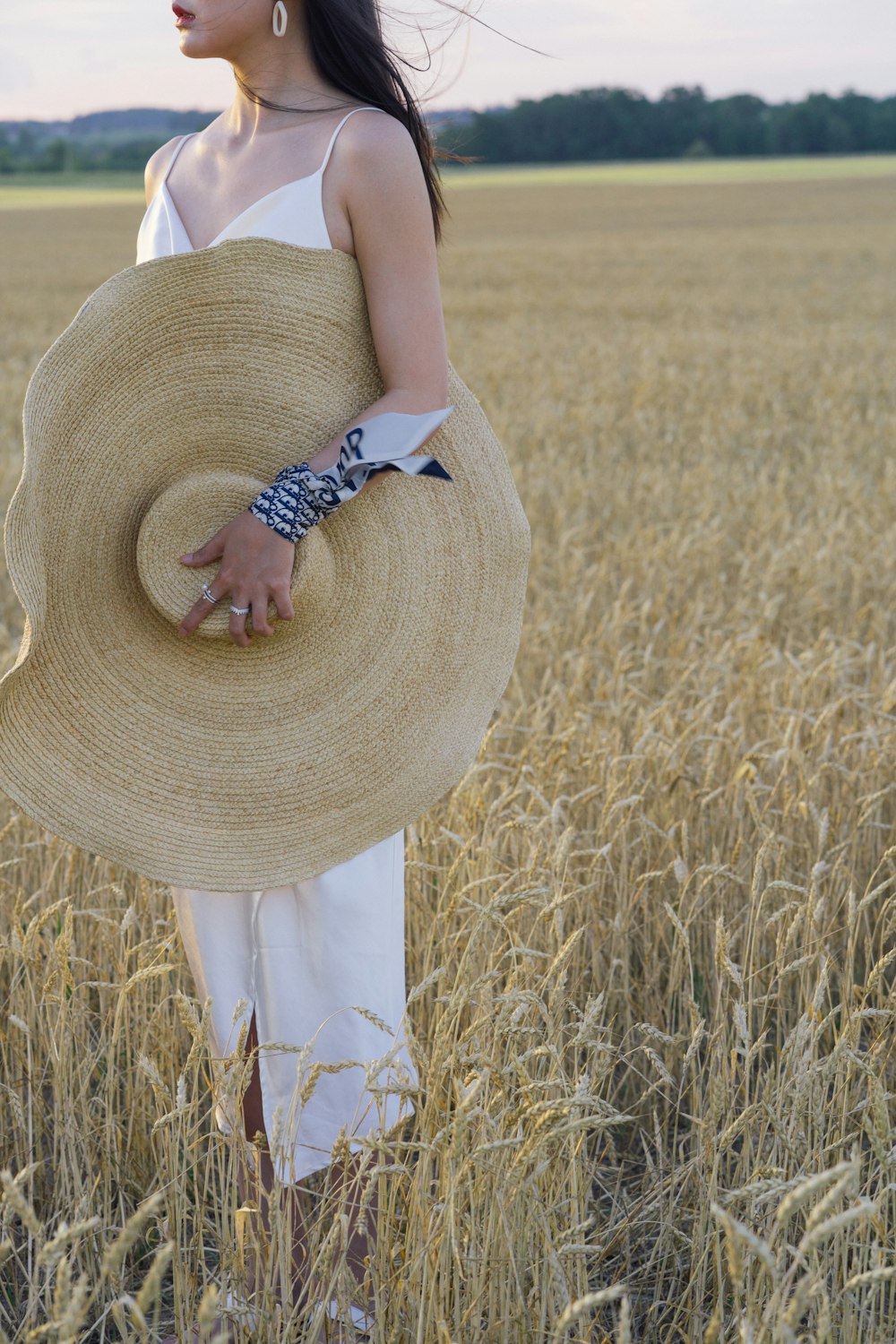 woman in white tank top and white skirt wearing brown sun hat standing on brown grass
